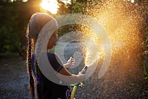 Child playtime outdoors with a water hose at sunset, creating a magical summer scene.