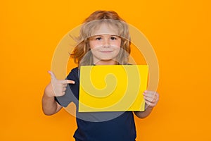 Child point on empty yellow sheet of paper, isolated on yellow background. Portrait of a kid holding a blank placard