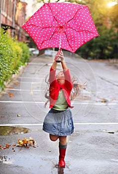Child with polka dots umbrella wearing red rain boots