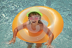 Child in pool on inflatable ring. Kid swim with orange float. Healthy outdoor sport activity for children.