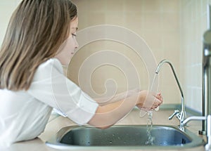 Child pouring fresh reverse osmosis purified water in kitchen at home. Drinking tap water. Consumption of tap water contributes to
