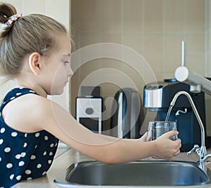 Child pouring fresh reverse osmosis purified water in kitchen at home. Drinking tap water. Consumption of tap water contributes to