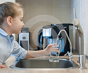 Child pouring fresh reverse osmosis purified water in kitchen at home. Drinking tap water. Consumption of tap water contributes to