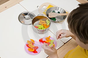 The child prepares toy food in the toy kitchen.