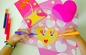 Child preparing for Mothers Day, making greeting card. Girl making paper sun and fabric crochet heart as gifts for Mothers day,