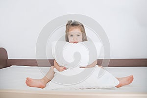 Child preparing to sleep sitting on bed with pillow on white