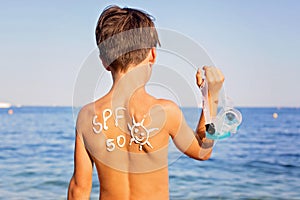 Child, preteen boy with sun protection cream on his back on the beach