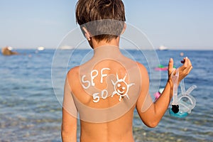 Child, preteen boy with sun protection cream on his back on the beach