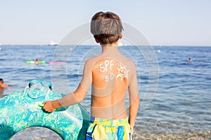 Child, preteen boy with sun protection cream on his back on the beach