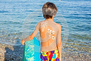 Child, preteen boy with sun protection cream on his back on the beach