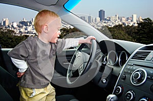 Child Pretends to Drive Car in Big City