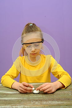 Child with protective eyeglasses makes science experiment at home with water and crystals