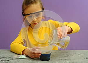 Child with protective eyeglasses makes science experiment at home with water and crystals