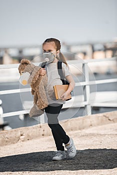child in protective mask holding teddy bear and book on bridge air