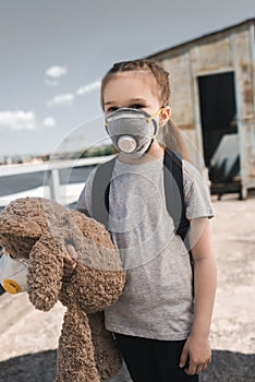 child in protective mask holding teddy bear on bridge air