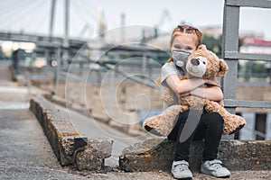 child in protective mask hugging teddy bear on street air
