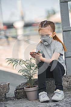 child in protective mask touching green potted plant air