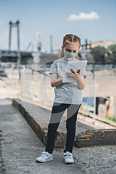 child in protective mask using tablet on street air