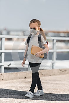 child in protective mask walking with book on bridge air