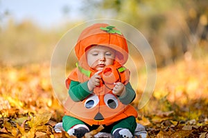 Child in pumpkin suit on background of autumn leaves