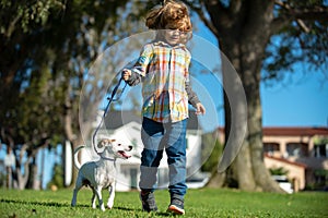 Child and puppy outside. Happy Kid boy and dog running at backyard lawn. Pet walking.