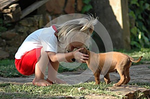 Attiva piccolo biondo caucasica bambino bambina di abbracciare il suo giovane cane, un Rhodesian Ridgeback dog cucciolo animale, in giardino, tenendo la sua testa.