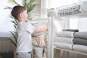 The child puts the bedding in a closet with neatly folded things. vertical storage.