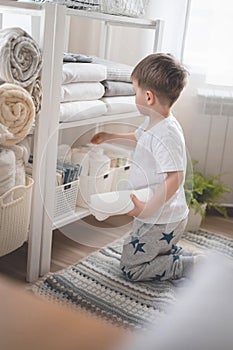 The child puts the bedding in a closet with neatly folded things. vertical storage.