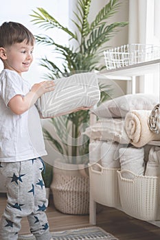 The child puts the bedding in a closet with neatly folded things. vertical storage.