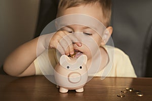 Child puts coins in piggy bank. Smart happy boy saving money in a piggy bank, learning about saving. Money, finances