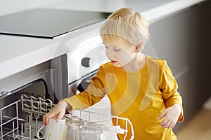 Child puts dirty crockery in the home dishwasher. Close-up