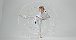 The child puts his hands on his belt and raises his leg high in the air. A girl who practices karate.