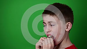 The child puts a plate on the teeth, slow motion, side view of a child, a boy on a green background.