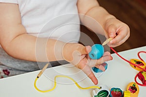 Child putting beads on a string. Bead stringing activity. Fine motor skills development