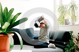 Child putting on black-white 3D Virtual Reality glasses sitting on sofa