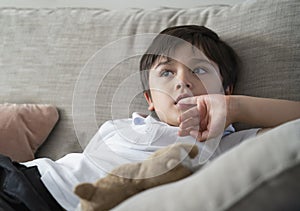 Child putting finger in his mouth. Schoolboy biting his finger nails while watching TV, Emotional kid portrait, Young boy siting