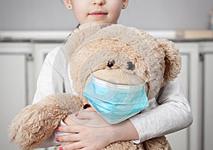 Child on quarantine due epidemic of coronavirus COVID-19. Child girl cuddle toy bear wear medical mask