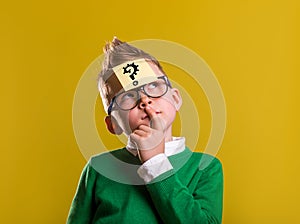 Child with question mark on sticker on forehead. Thinking kid in glasess against yellow background. Back to school
