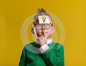 Child with question mark on sticker on forehead. Thinking kid in glasess against yellow background. Back to school.