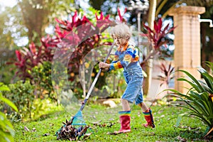 Child and rake in autumn garden. Kid raking leaves