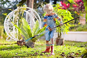 Child and rake in autumn garden. Kid raking leaves