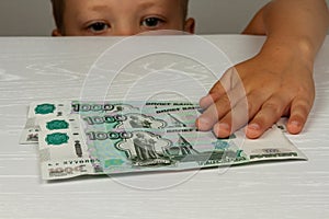 The child reaches for money lying on a wooden table