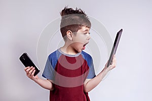 Child reacting to a tablet and holding a cell phone