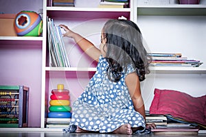 Child read, cute little girl selecting a book on bookshelf