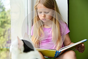 Child reading a book in the afternoon at the window