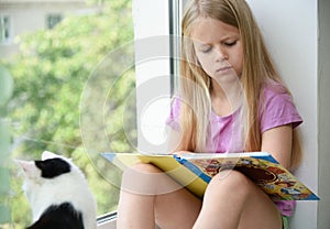 Child reading a book in the afternoon at the window