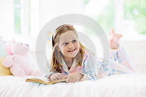 Child reading book in bed. Kids read in bedroom