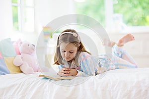Child reading book in bed. Kids read in bedroom