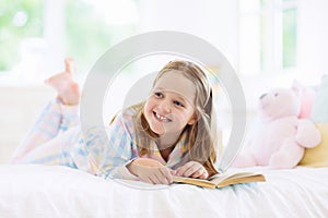 Child reading book in bed. Kids read in bedroom