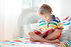 Child reading book in bed. Kids read in bedroom